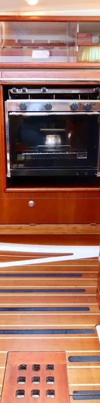Een houten bootinterieur toont een kombuis met een ingebouwde oven, kasten, laden en een houten vloer met treden.