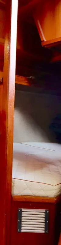 De foto toont een houten bootinterieur met een bed, een marifoon, schakelpanelen, meters en een trap.