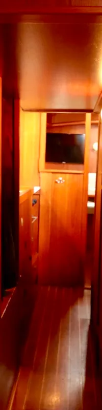 Een houten gang met een witte gordijn aan de rechterkant, een grijze matras en een tv-scherm verderop.