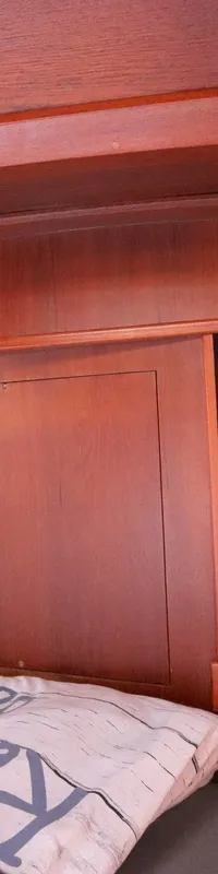 Een houten kajuitinterieur met een bed, opbergvakken, een plafond met inbouwspots en een klein elektrisch kastje.