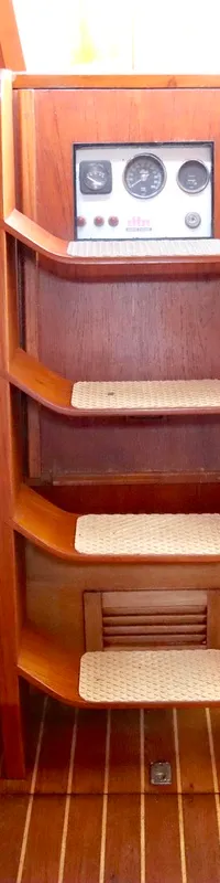 Een houten scheepstrap met drie treden en een instrumentenpaneel erboven is zichtbaar in een houten interieur.