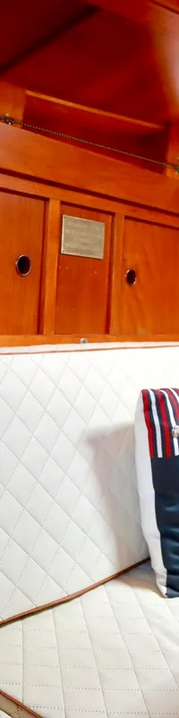 Een houten interieur met witte gestikte kussens, decoratieve kussens, een houten tafel en een televisie is zichtbaar.