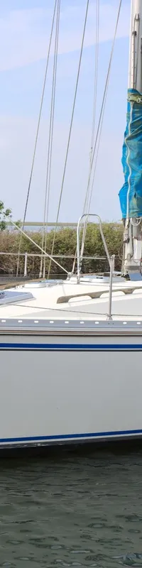 Een witte zeilboot met blauwe strepen en de naam "Golden Spirit" op de romp ligt in het water, met een blauwe sprayhood en…