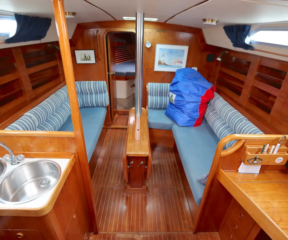 De kajuit van een boot toont een houten interieur met twee banken met blauwe kussens, een gootsteen en een tafel. — Moody 376