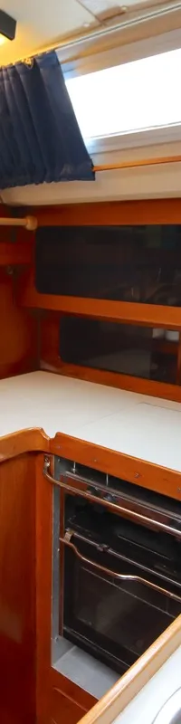 De kombuis toont een houten interieur met een wit aanrechtblad, dubbele spoelbak, kraan, ingebouwde oven en opbergplanken.