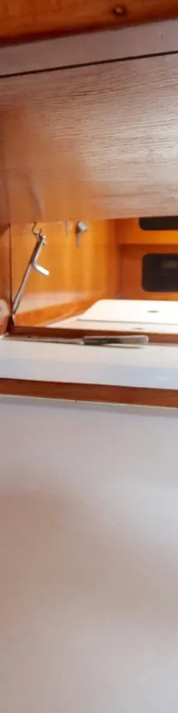 De foto toont een houten kajuitinterieur met een wit aanrechtblad, een zwart ventilatierooster en een fornuis/oven in de…