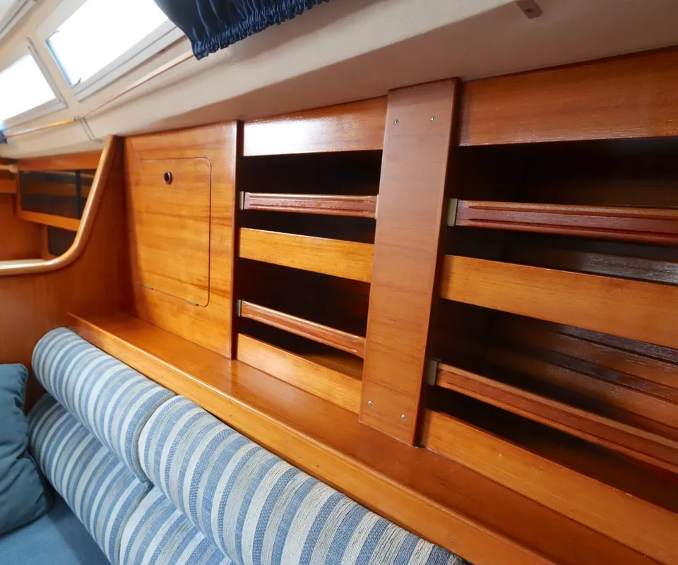 De kajuit toont een houten interieur met een bank met gestreepte kussens, opbergvakken en ramen met gordijnen. — Moody 376
