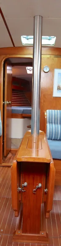 De kajuit van een boot toont een houten interieur met blauwe banken, een inklapbare tafel en een maststeun. — Moody 376
