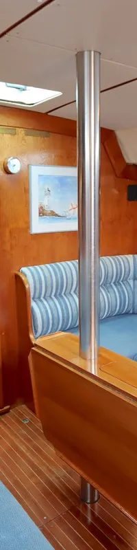 De kajuit toont een houten interieur met blauwe zitkussens en gestreepte rugkussens, een opklapbare tafel en een doorgang…