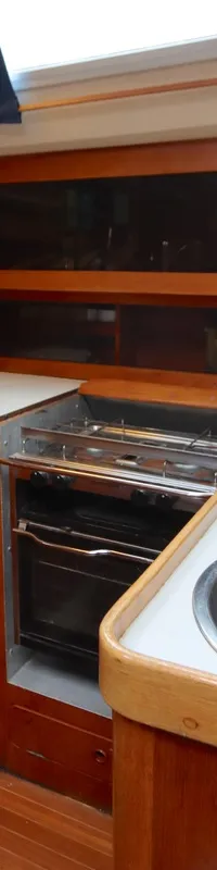 Een houten kajuitinterieur met een kombuis voorzien van twee RVS spoelbakken, een kraan en een gasfornuis met oven.