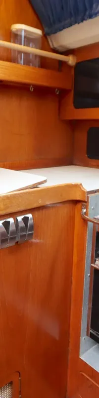 Een scheepskeuken met houten betimmering, een gasfornuis met oven, een werkblad, opbergruimte en een flesopener.