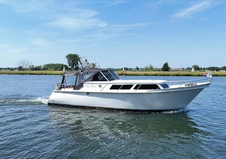 Een witte motorboot met een zwarte kap vaart op een blauwe waterweg onder een heldere hemel. — Valk Sport