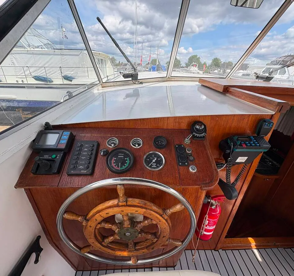 Een houten stuurwiel en dashboard met diverse meters, knoppen en navigatieapparatuur zijn zichtbaar.
