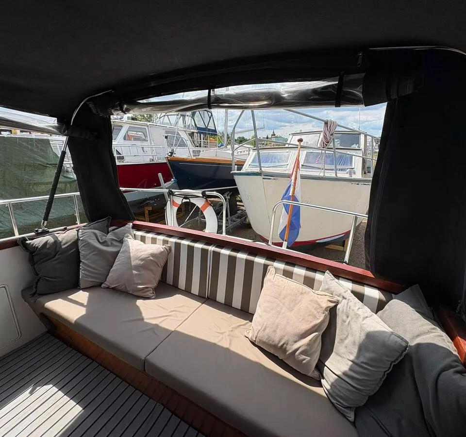 Een bootinterieur met een bank met kussens en een gestreepte rugleuning, met uitzicht op andere boten.