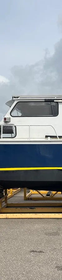 Een blauw-witte motorboot met de naam "Kira" op de boeg staat op gele bokken onder een bewolkte hemel. — Altena GSAK