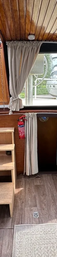 De kajuit toont een houten plafond, twee blauwe banken, een houten rek, ramen met gordijnen en een brandblusser.