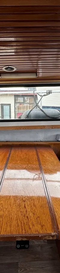 De boot heeft een houten interieur met blauwe zitkussens, een houten tafel en ramen met gordijnen. — Altena GSAK