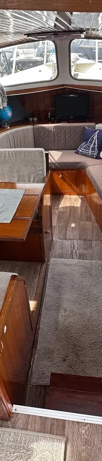 De foto toont het interieur van een boot met houten afwerking, een zithoek met tafel, een kombuis met spoelbak en…