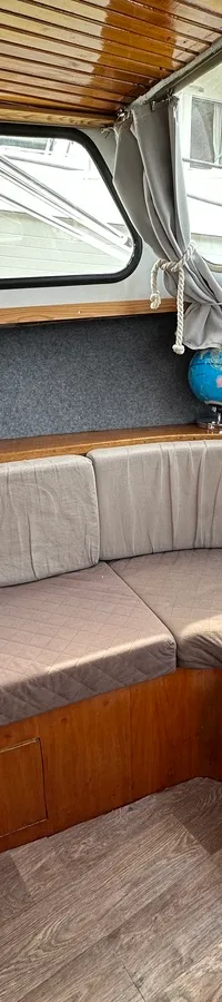 De foto toont een bootinterieur met een U-vormige bank, houten afwerking, ramen met gordijnen, een tv en een globe.