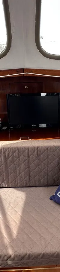 De foto toont een interieur van een boot met een gebogen zitbank, twee decoratieve kussens, een televisie, een wereldbol en…