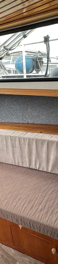 Een L-vormige bank met grijze kussens en twee nautische sierkussens is zichtbaar in een houten interieur met ramen.