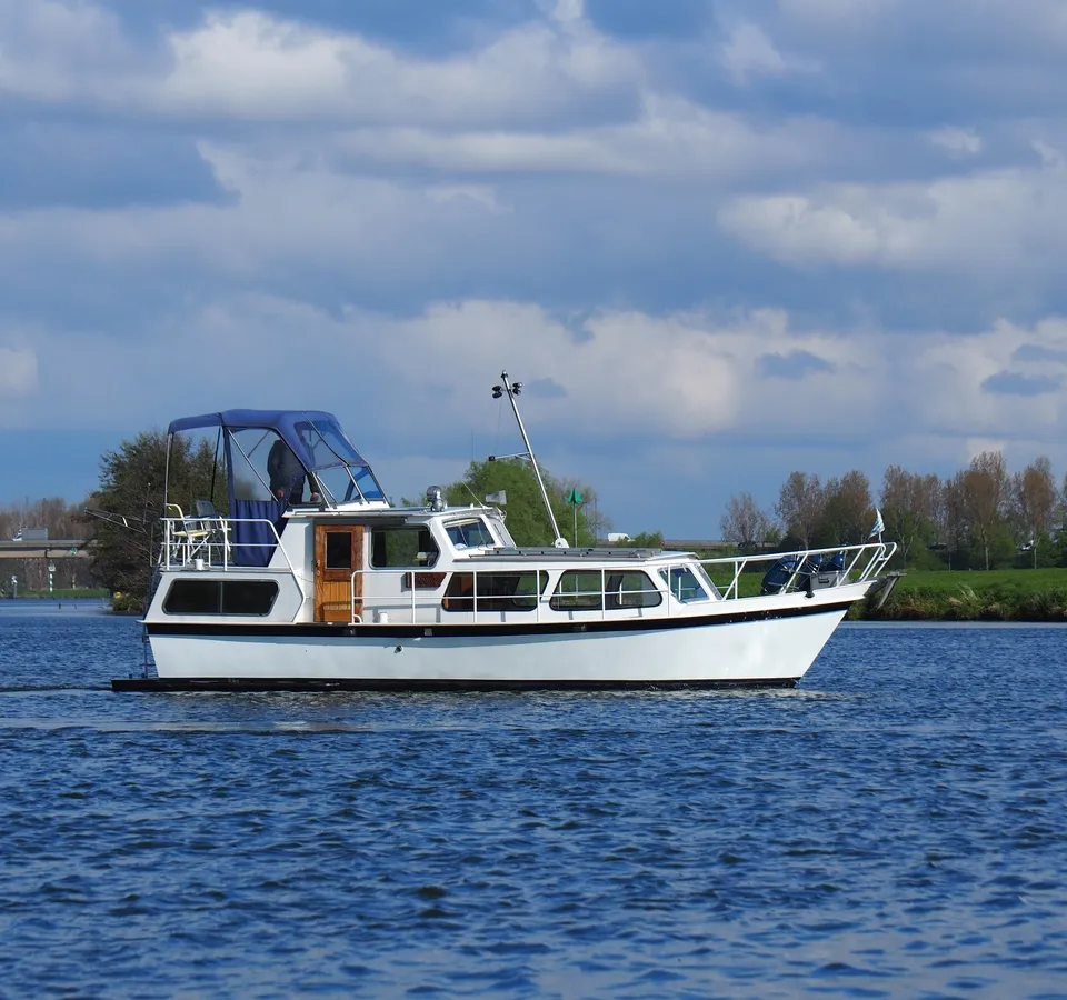 Een witte motorboot met blauwe kap vaart op het water onder een bewolkte hemel. — Cascaruda 920