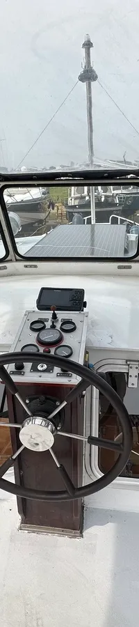 De foto toont het stuurgedeelte van een boot met een stuurwiel, instrumentenpaneel en een voorruit met meerdere ramen.
