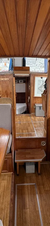 De foto toont het interieur van een boot met houten wanden en plafond, een zithoek met tafel en een kombuis. — Cascaruda 920