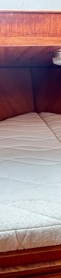 Een witte matras met een golvend patroon ligt in een houten kajuit met een lampje aan het plafond. — Cascaruda 920