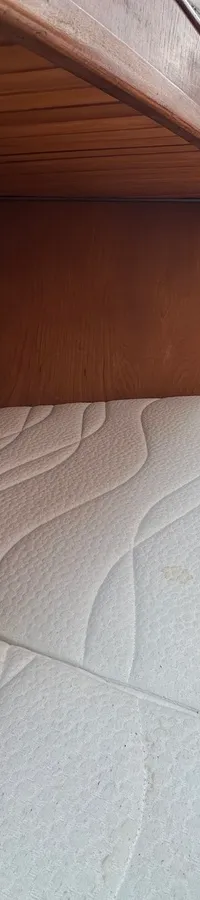 Een wit matras met patroon vult een houten kajuit, met een lamp aan het plafond en een wit gordijn. — Cascaruda 920