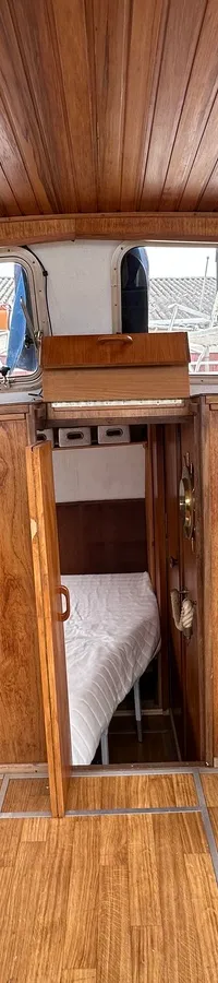 De foto toont het interieur van een boot met houten wanden, vloer en plafond, een bed en een kaart aan de muur.