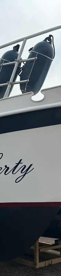 Een witte boot met de naam "Liberty" in zwarte letters, liggend op houten bokken naast een andere boot. — Cascaruda 920