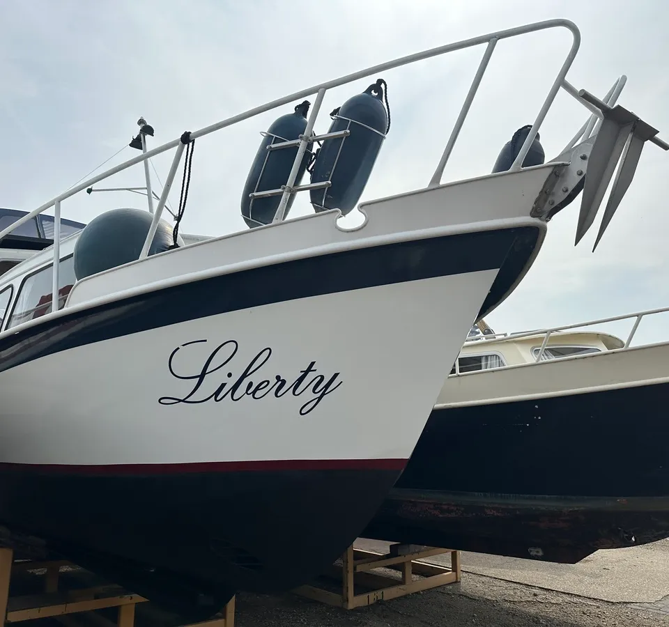 Een witte boot met de naam "Liberty" in zwarte letters, liggend op houten bokken naast een andere boot. — Cascaruda 920