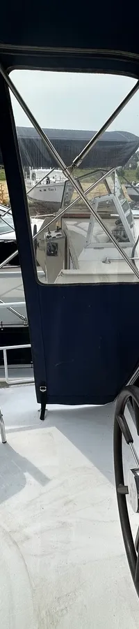 Een bootdek met een stuurwiel, instrumentenpaneel, een Garmin-apparaat, een witte stoel en een uitzicht op andere boten en…
