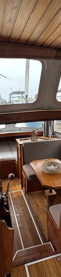 Een houten stuurhut met een stuurwiel, navigatie-instrumenten, een zithoek en uitzicht op andere boten.