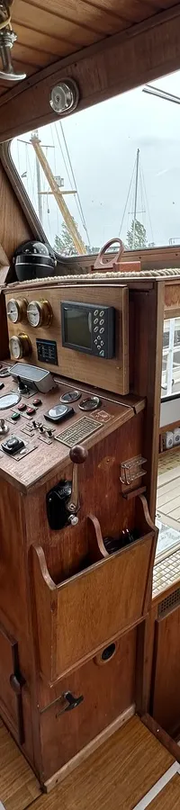 De foto toont het interieur van een boot met een houten stuurwiel, dashboard, kombuis en zitgedeelte. — Cascaruda 920