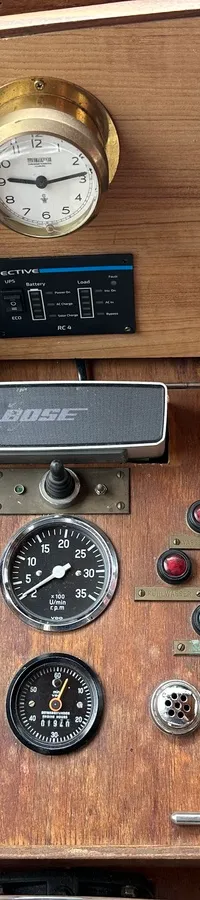 Een houten dashboard met diverse meters, schakelaars, een GPS-navigator, een Bose-luidspreker en een verwarmingsregelaar.