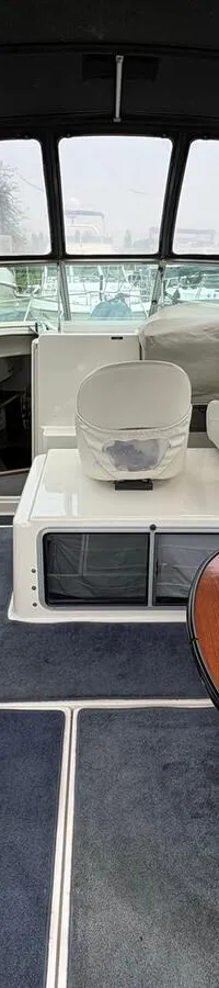 De foto toont het interieur van een boot met een donkerblauw tapijt, witte banken en een bruine ovale tafel. — Maxum 3200 SCR