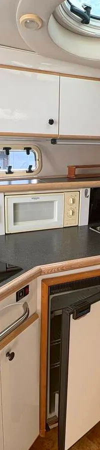 De foto toont de cockpit van een boot met een stuurwiel, instrumentenpaneel, twee witte stoelen en een uitzicht op andere…