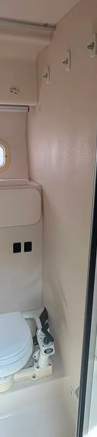 Een witte boot met zwarte accenten en een zwarte kap staat op een blauwe trailer op een geasfalteerd terrein onder een…