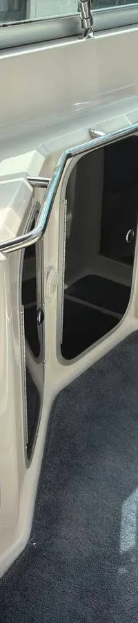 Een witte motorboot met een zwarte kap en doorzichtige ramen staat op het droge, met twee schroeven zichtbaar aan de…