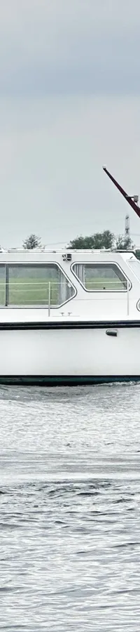 Een witte motorboot met de naam "Silver Lining" vaart op het water, met een groene oever en bomen op de achtergrond.
