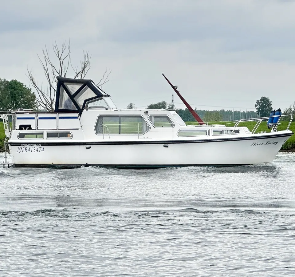 Een witte motorboot met de naam "Silver Lining" vaart op het water, met een groene oever en bomen op de achtergrond.