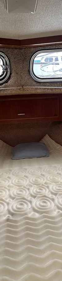 De foto toont een kajuit met een beige tapijt, twee ramen met gordijnen en een bed met een wit schuimmatras. — Neptunus 107