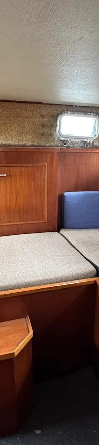 Een kajuit met houten wanden, twee banken met grijze kussens en meerdere ramen. — Neptunus 107