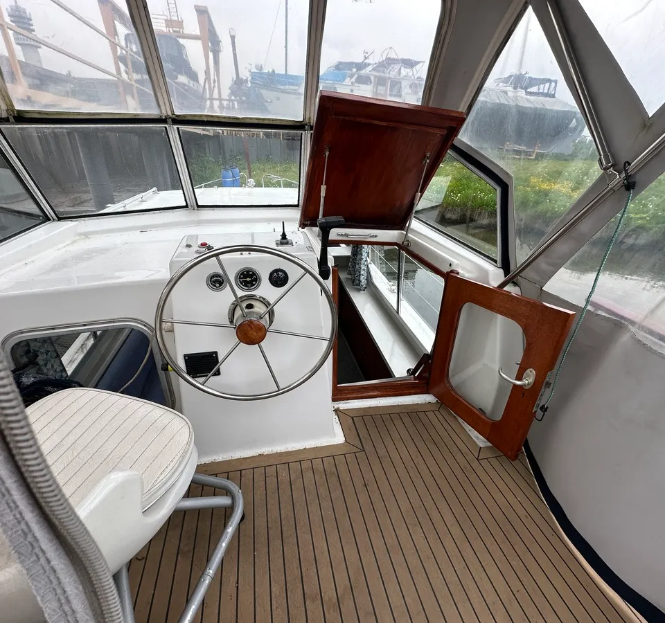 De foto toont het interieur van een boot met een stuurwiel, instrumentenpaneel, een stoel en een houten vloer. — Neptunus 107