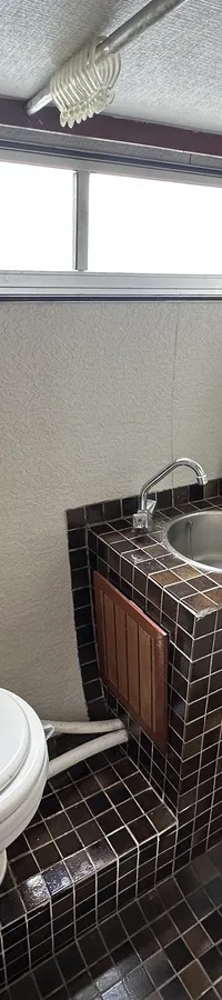 De foto toont een badkamer met een toilet, een wastafel met kraan en een douchekop, en een raam.