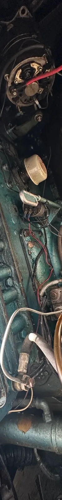 Een close-up van een blauwgroene scheepsmotor met diverse slangen, kabels en onderdelen in een motorruimte.