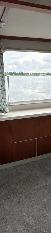 De foto toont het interieur van een boot met een bar, twee barkrukken, een tafel, ramen met uitzicht op water en land, en…