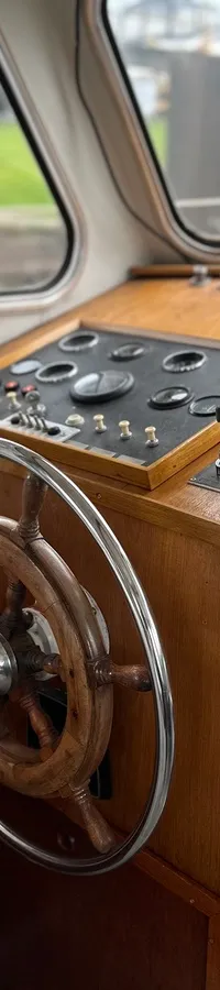 Een houten stuurwiel en bedieningspaneel met diverse meters en schakelaars zijn zichtbaar in de stuurhut van een boot.
